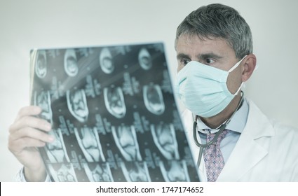 Male Doctor In His Office Wearing Mask Looking At Xray Scan.