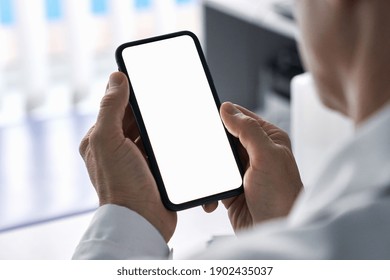 Male doctor holding cell phone in hands using blank white mockup screen technology ehealth mobile app for medical healthcare telemedicine ads, e telehealth online applications. Over shoulder view - Shutterstock ID 1902435037