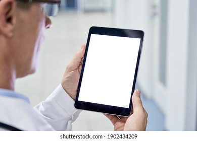 Male doctor holding digital tablet in hands using blank white mockup screen technology for medical healthcare tech website ads concept, video call e telehealth online appointment. Over shoulder view
