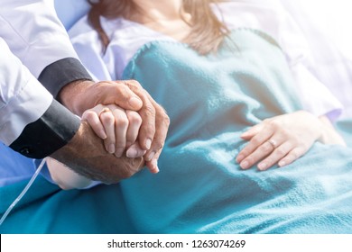 Male Doctor Holding Female Patient Hand On The Hospital Bed.