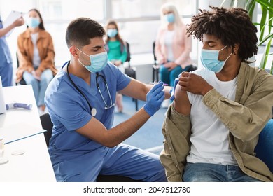 Male doctor holding syringe making covid 19 vaccination injection dose in shoulder of black male patient. Flu influenza vaccine clinical trials concept, corona virus treatment side effect, inoculation - Powered by Shutterstock