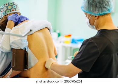 Male doctor injecting Epidural Anesthesia for pregnancy Labor during childbirth for woman pathient in hospital. Spinal anesthesia. Doctor makes a puncture in the lumbar spine
