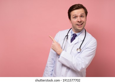 Male Doctor Makes A Pointing Finger Gesture, Isolated Over A Pink Background