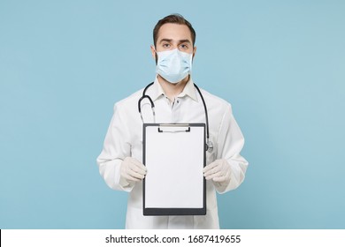 Male doctor man in medical gown face mask gloves isolated on blue background. Epidemic pandemic coronavirus 2019-ncov sars covid-19 flu virus concept. Hold clipboard with blank empty sheet workspace - Shutterstock ID 1687419655
