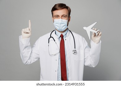 Male doctor man wear white medical gown suit mask work in hospital hold airplane mock up point index finger overheadisolated on plain grey color background studio portrait. Healthcare medicine concept - Shutterstock ID 2314931555