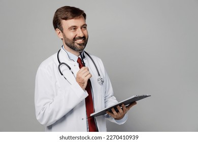 Male doctor man wears white medical gown suit work in hospital hold clipboard with paper documents prop up chin look aside on workspace isolated on plain grey background Healthcare medicine concept - Shutterstock ID 2270410939