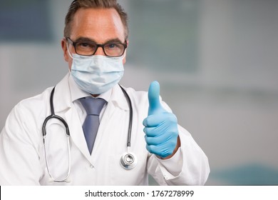 male doctor with medical face mask, medical gloves and a stethoscope shows thumbs up