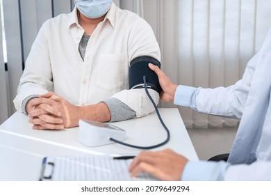 Male Doctor In Medical Face Mask Is Using Sphygmomanometer To Checking Blood Pressure To Male Patient And Taking Note Data On Clipboard In Clinic