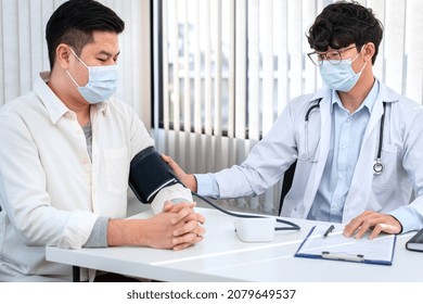 Male Doctor In Medical Face Mask Is Using Sphygmomanometer To Checking Blood Pressure To Male Patient And Taking Note Data On Clipboard In Clinic