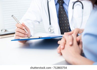 Male Doctor Noting A Female Patient Medical Check Up Information In Hospital
