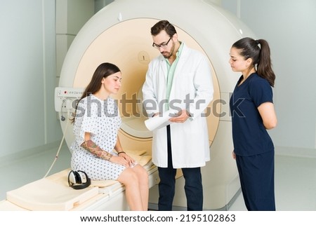 Male doctor and nurse showing the exam results to a female patient sitting on the MRI machine at the medical imaging center