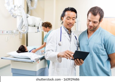 Male Doctor And Nurse Using Digital Tablet While Colleague Preparing Patient For Xray In Examination Room