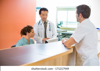 Male doctor and nurse using digital tablet while patient standing at reception desk in hospital