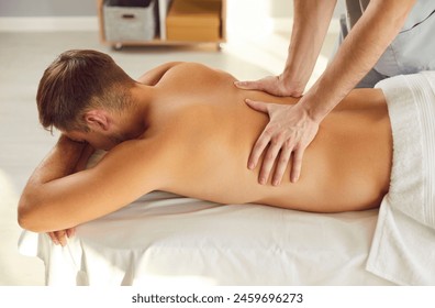 Male doctor osteopath or physiotherapist helping young male patient lying on the couch in modern rehab clinic with healing back pain making him medical massage. Physiotherapy concept. - Powered by Shutterstock