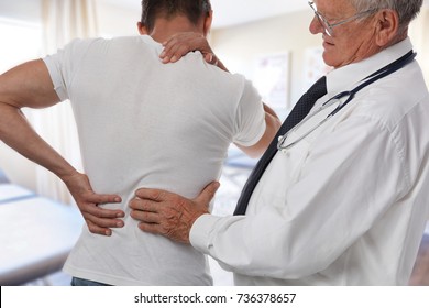 Male Doctor And Patient Suffering From Back Pain During Medical Exam.