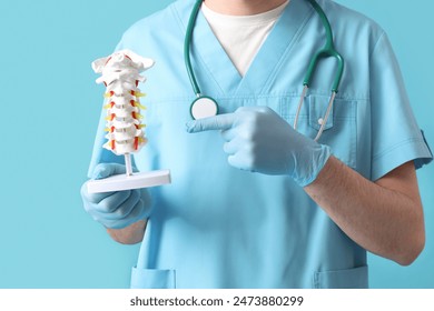 Male doctor pointing at spine model on blue background - Powered by Shutterstock