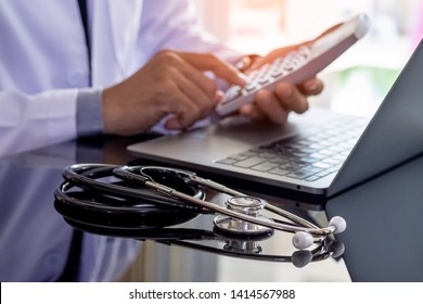 Male Doctor Or Practitioner Using Calculator And Work On Laptop Computer With Medical Stethoscope On The Desk At Clinic Or Hospital. Medical Healthcare Costs ,fees And Revenue Concept.