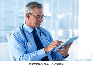 Male Doctor Reviewing Data On Digital Tablet In Clinic