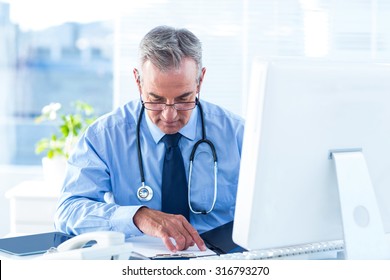 Male doctor reviewing document at desk in hospital - Powered by Shutterstock