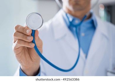 Male doctor showing stethoscope for checkup. Close up of doctor hand holding stethoscope to auscultate breath. Doctor with stethoscope in hand on hospital background for medical visit.