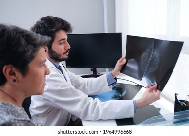 A Male Doctor Sits At His Desk And Talks To A Female Patient While Looking At Her Mammogram. Brest Cancer Prevention.