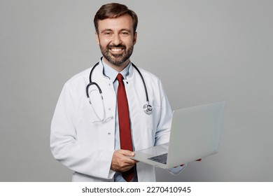 Male doctor smiling IT man wears white medical gown suit stethoscope work in hospital hold use laptop pc computer isolated on plain grey color background studio portrait. Healthcare medicine concept - Shutterstock ID 2270410945