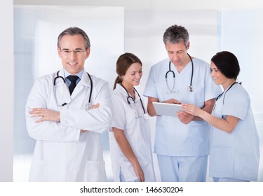 Male Doctor Standing In Front Of Team Using Digital Tablet