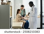 Male doctor standing near seated child and mother in clinic room. Child holding stuffed toy while doctor explaining something to them