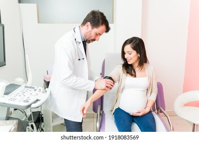 Male doctor taking the blood pressure of a pregnant woman for a routine check up. Healthy pregnant woman sitting at the examination room at the consulting room of the gynecologist