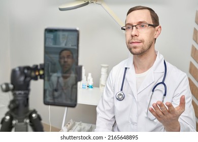 Male Doctor Talk To Patients By Phone. Telemedicine Content. Tripod Holds Camera. Blogger Therapist. Telehealth Media Record. Internet Clinic Speech. Hospital Webinar Office