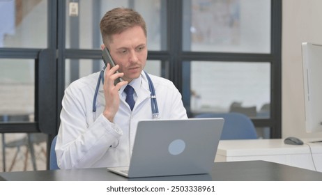 Male Doctor Talking on Phone and Using Laptop - Powered by Shutterstock