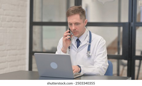 Male Doctor Talking on Phone and Using Laptop - Powered by Shutterstock