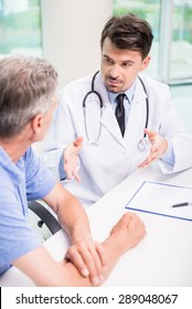 Male Doctor Talking With Patient Seriously At Clinic.