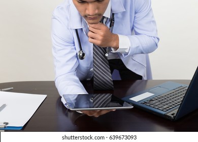 Male Doctor Thinking And Working With Modern Digital Tablet Or Touchpad And Laptop Computer At Workplace - Medical Technology Concept.