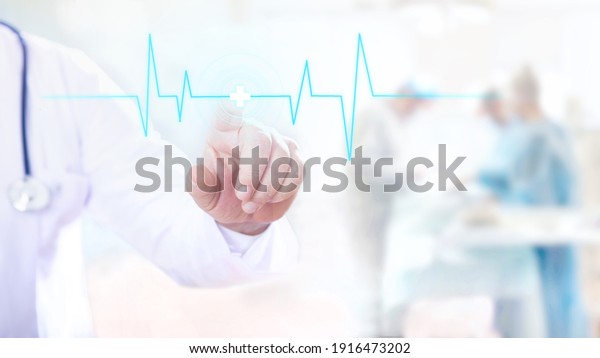 Male doctor touches a digital transparent
screen with pulse rhythm. Doctors make operation in operating room
on the background.