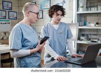 Male Doctor Using Computer And Talking To His Colleague, They Discussing Working Moments At Vet Clinic