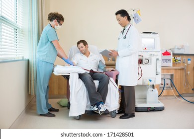 Male doctor using digital tablet with nurse setting up renal dialysis on patient in hospital room