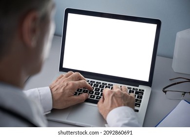 Male doctor using laptop computer with blank white mockup screen technology for tele medicine medical healthcare tech website ad concept, video call e telehealth online appointment. Over shoulder view