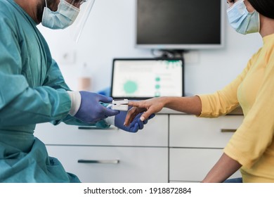 Male doctor using pulse oximeter on woman patient finger while wearing surgical face masks for coronavirus outbreak - Measuring oxygen saturation - Shutterstock ID 1918872884