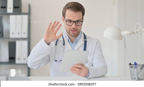 Male Doctor Waving Hand For Video Chat On Tablet