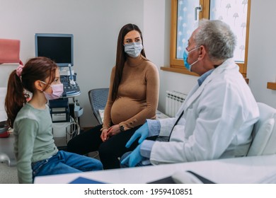 Male Doctor Wear Protection Face Mask Talking With Patient In Clinic Office While Her Mother Sitting Beside Them