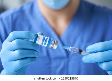 Male doctor wearing blue uniform, mask, medical gloves holding syringe taking covid 19 corona virus vaccine from vial bottle preparing for injection. Coronavirus immunization flu treatment vaccination