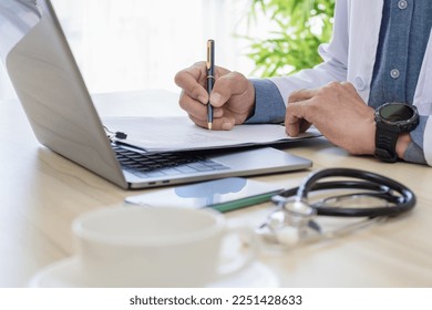 Male doctor in white coat hand writing medical document on clipboard with laptop computer and medical stethoscope on the desk at clinic or hospital. - Powered by Shutterstock