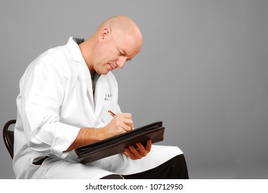 Male doctor in white coat looking serious while making notes