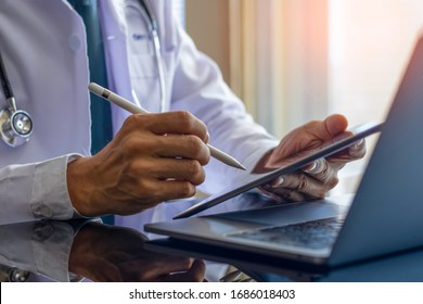 Male doctor in white coat with  medical stethoscope, hand holding and using modern digital tablet, work on laptop computer at office. Telehealth, Online medical networking concept. 