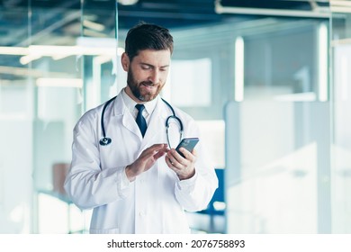 Male doctor in a white coat in a modern clinic reads information from a mobile phone corresponds with colleagues happy and smiles - Powered by Shutterstock