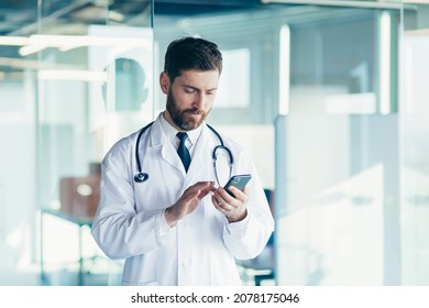 Male doctor in a white coat in a modern clinic reads information from a mobile phone corresponds with colleagues happy and smiles - Powered by Shutterstock