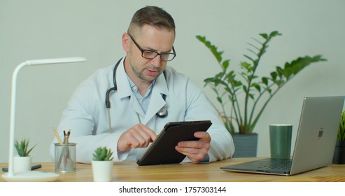 Male doctor in white coat using modern TabletPC device with touch screen. Doctor using DigitalTablet texting to patient informing about medical test results.