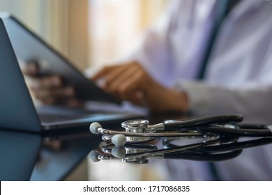 Male Doctor In White Lab Coat Hand Holding And Using Modern Digital Tablet, Work On Laptop Computer With  Stethoscope On The Desk At Workplace. Medic Tech,e Health, Online Medical Or Ehr Concept. 