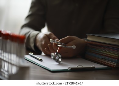 Male Doctor In White Lab Coat Reading Text Book, Search Information And Working On Laptop Computer With  Medical Stethoscope On The Desk In Room At Clinic. Medical Knowledge And Education Concept.